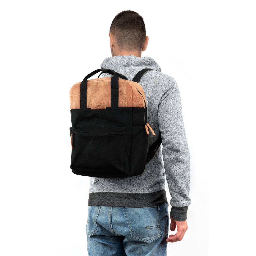 Rückansicht junger Mann mit hellem Pullover und Rucksack aus schwarzem Stoff mit hellen Korkteilen auf dem Rücken