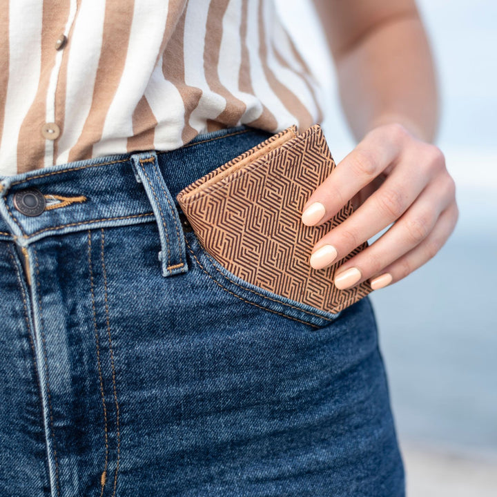 Frau in blauer Jeans steckt kleine Kork Geldbörse mit dunklem Gittermuster in die vordere linke Hosentasche #color_vinicunca