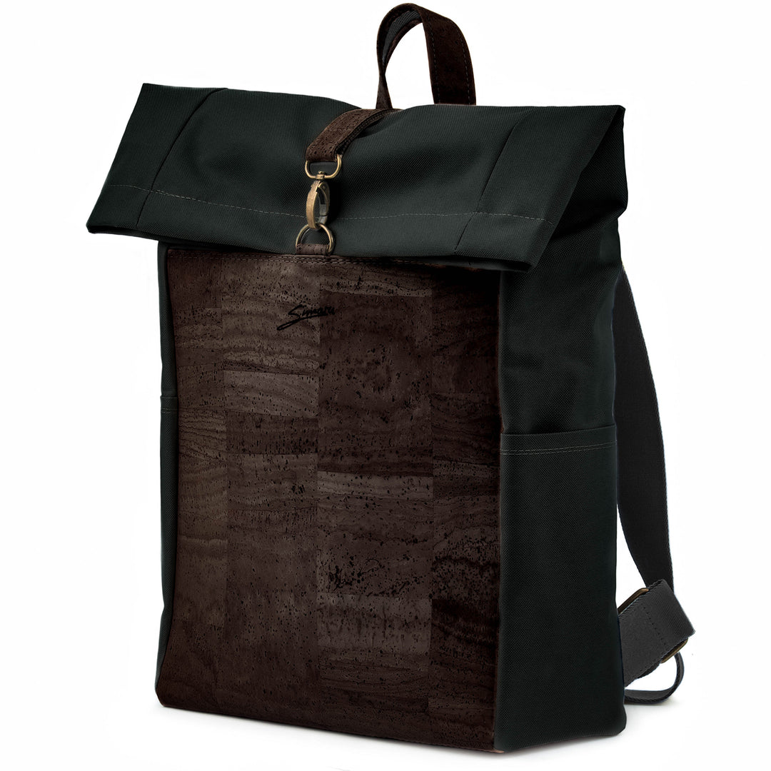 Leicht seitliche Ansicht geschlossener Rolltop Rucksack mit dunkelbrauner Kork Front und schwarzem Stoff mit Karabinerverschluss, breiten Stoffträgern und Tragegriff aus Kork