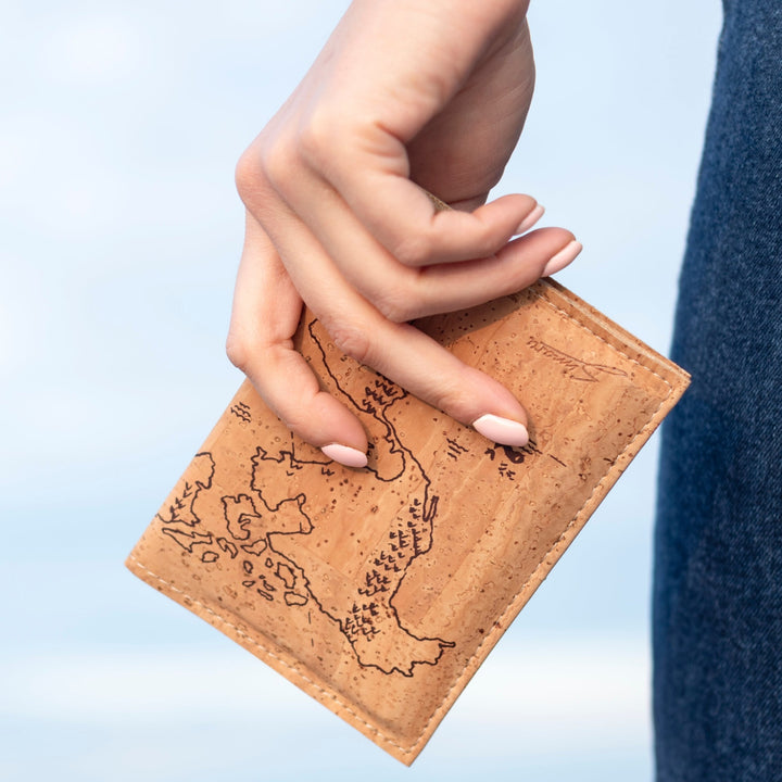 Frau hält Reisepasshülle aus Kork mit aufgedruckter Weltkarte in der Hand