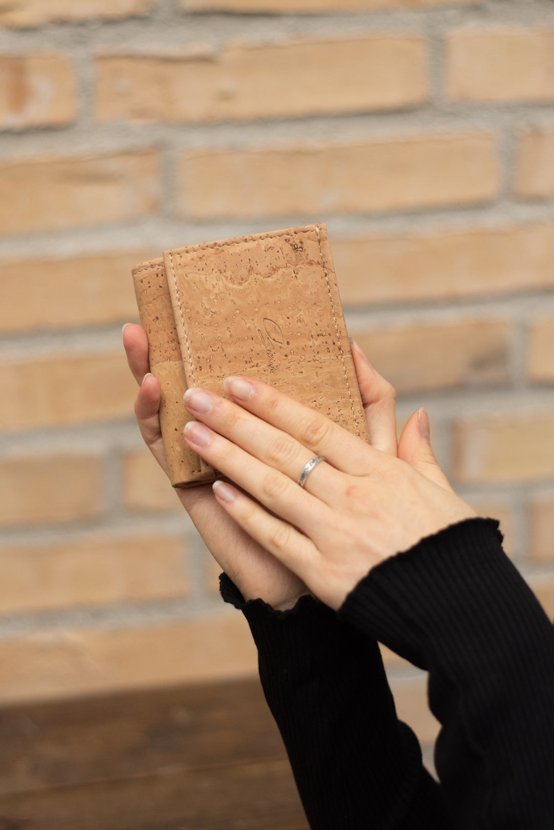 Damenhände halten kleine Kork Geldbörse in der Farbe beige vor einer Wand im Hintergrund #color_schwarz