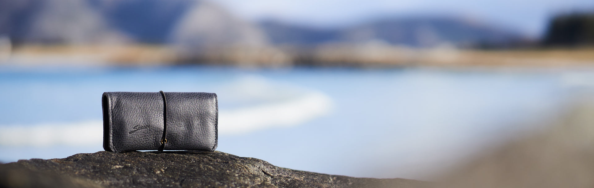 Schwarze Tabaktasche aus Leder stehend auf Fels am Meer