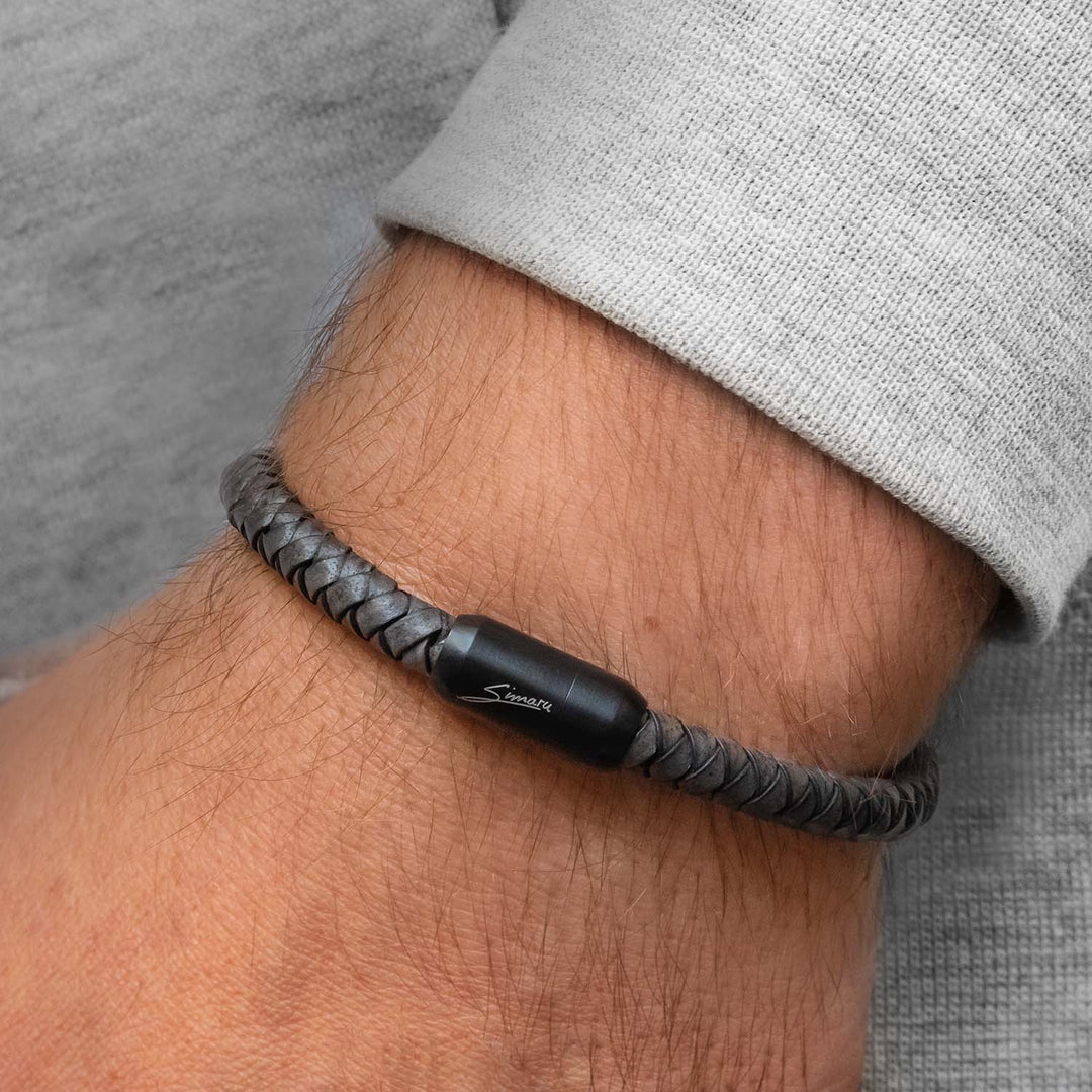 Graues, geflochtenes Lederarmband mit schwarzem Magnetverschluss um Herrenhandgelenk