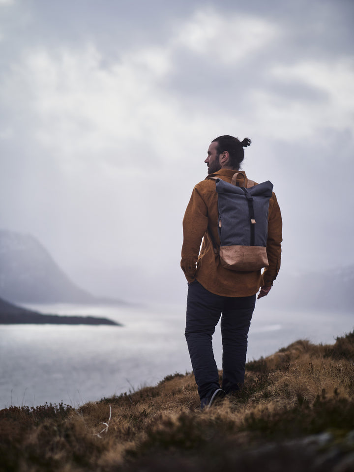 Junger Mann trägt grauem Rucksack mit hellem Korkboden beim Wandern an der Küste 