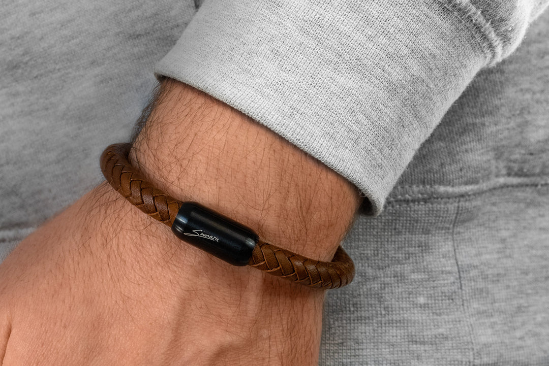 Breit geflochtenes, braunes Lederarmband mit schwarzem Magnetverschluss um Herrenhandgelenk