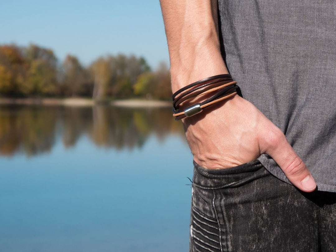 Mann mit braunem Wickelarmband aus Leder am rechten Handgelenk posiert vor einem See