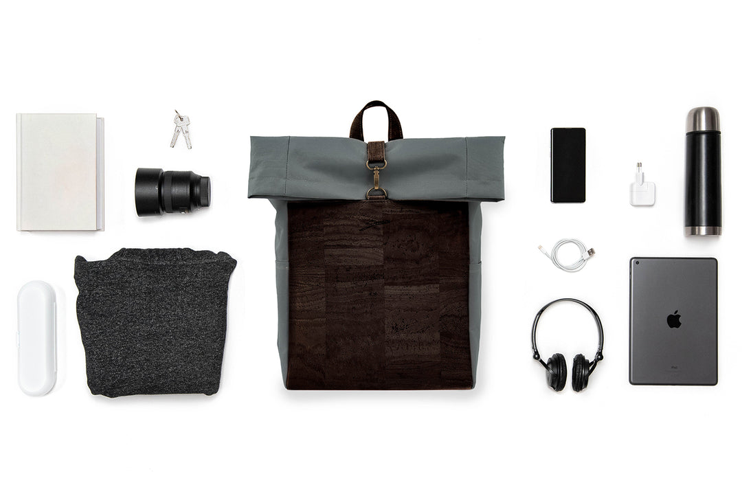 Collage mit grauem Toploader Rucksack mit dunkelbrauner Korkfront im Zentrum und ausgebreitetem Inhalt wie Kamera Equipment, Laptop, Trinkflasche etc. drum herum 