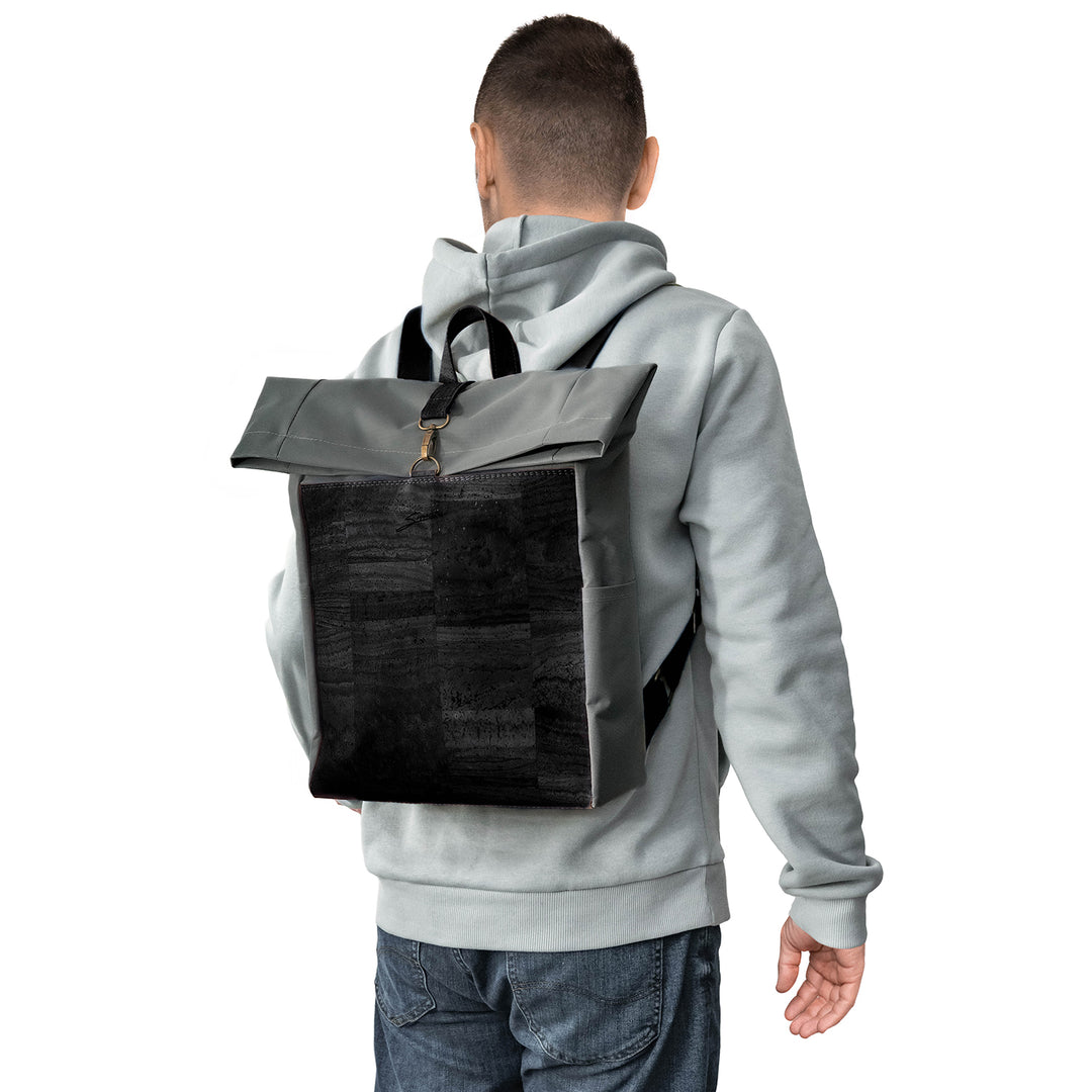 Rückansicht junger Mann mit hellem Pullover und Rucksack aus grauem Stoff mit schwarzer Korkfront auf dem Rücken