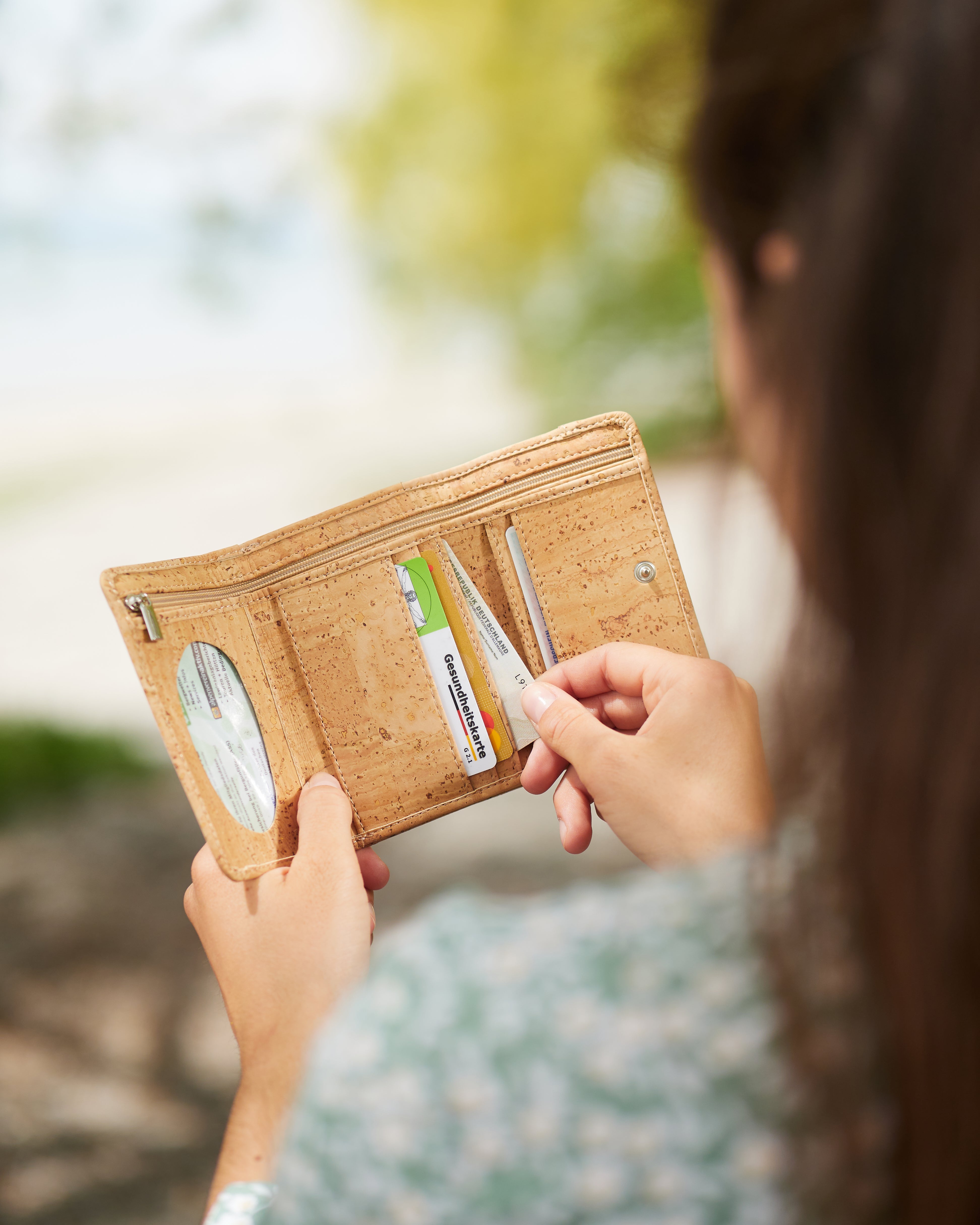 Schulterblick junge Frau zieht Geldkarte aus hellem Kork Portemonnaie