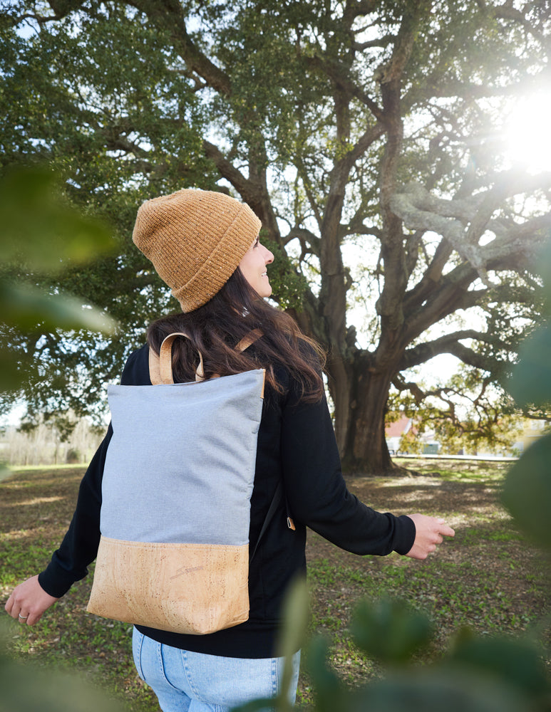 Junge Frau geht lächelnd mit Korkrucksack auf dem Rücken in der Natur spazieren