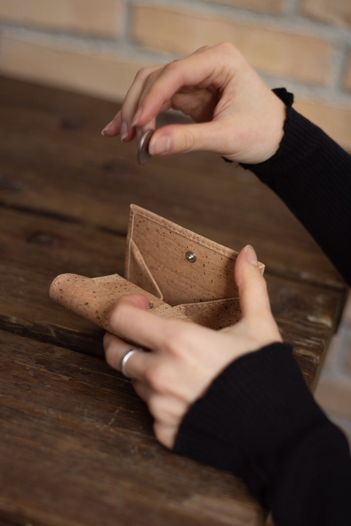 Damenhände nehmen Münze aus geöffneter Kork Geldbörse an einem Holztisch sitzend #color_beige