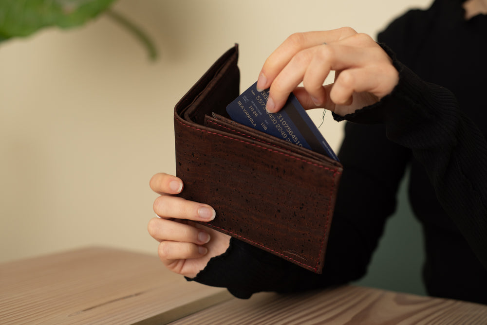 Person sitzt an Holztisch und nimmt Geldkarte aus geöffnetem dunklen Kork Portemonnaie