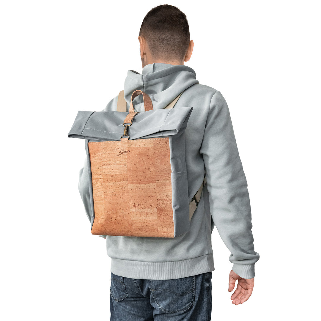 Rückansicht junger Mann mit hellem Pullover und Rucksack aus grauem Stoff mit heller Korkfront auf dem Rücken